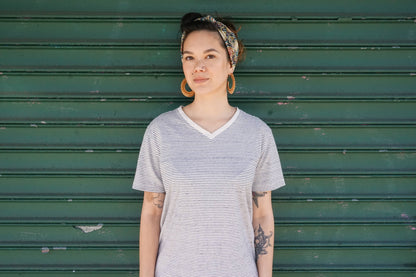 Young woman with short dark hair and tattoo wearing a striped t-shirt standing in front of a green wooden wall