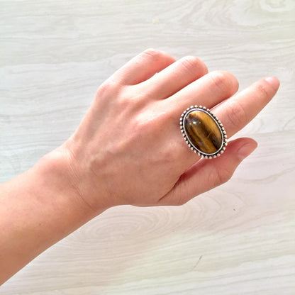 Vintage oval tiger's eye gemstone ring in sterling silver 925 setting worn on hand, close-up view on light wood background.