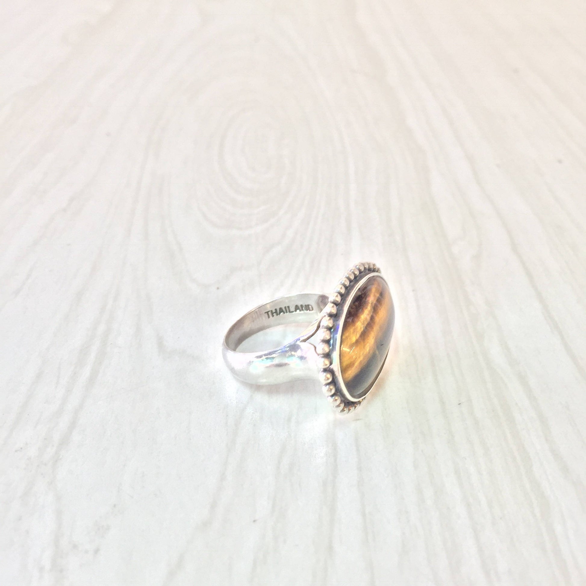 Sterling silver ring with an oval-shaped tiger's eye gemstone set in a bezel setting on a textured silver background.