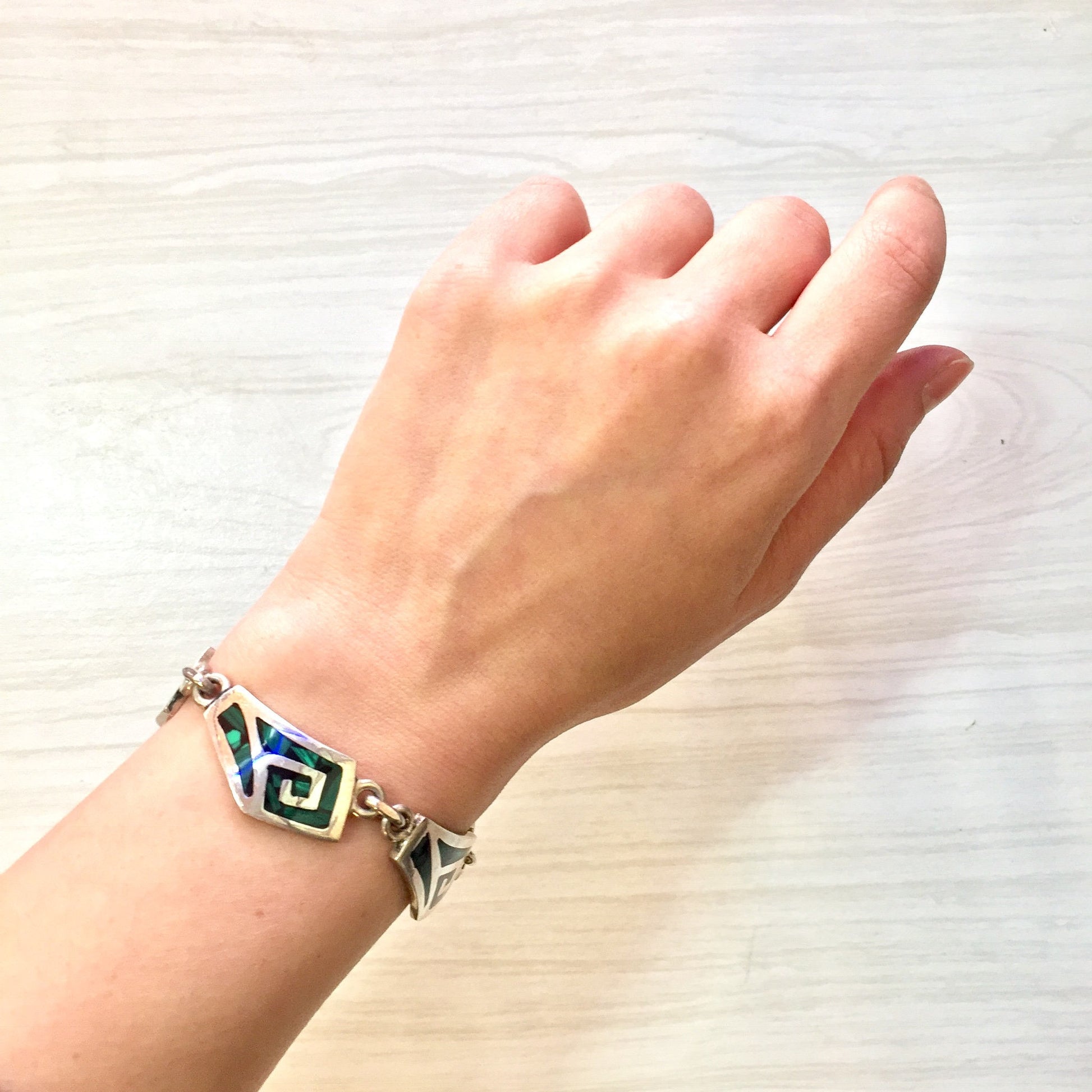 Vintage sterling silver link bracelet with inlaid green malachite gemstones on a wrist, against a light wooden background.