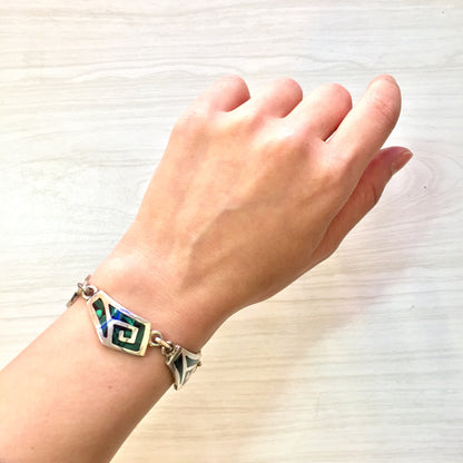 Vintage sterling silver link bracelet with inlaid green malachite gemstones on a wrist, against a light wooden background.