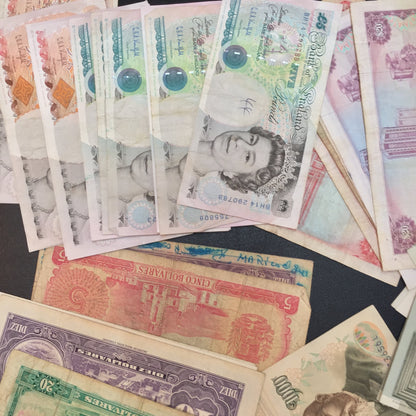 Vintage foreign currency banknotes in various denominations and colors, including British pounds, scattered on a surface for scrapbooking or craft projects