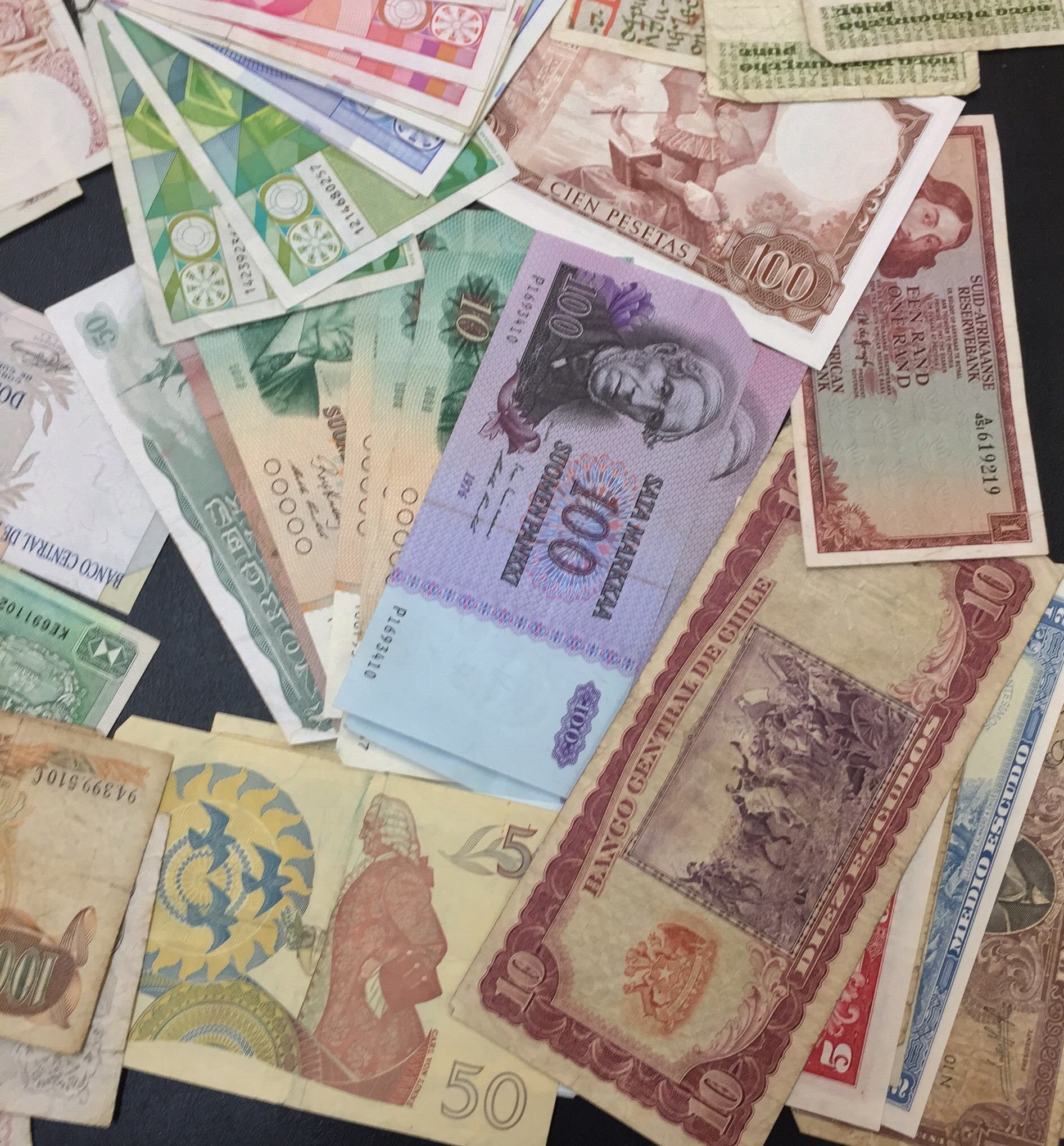 Vintage foreign currency banknotes from various countries scattered on a flat surface, featuring colorful designs and denominations for scrapbooking, crafting or collecting.