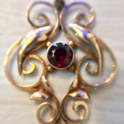 Antique 10K gold pendant featuring an intricate swirl design with a deep purple amethyst stone at the center and iridescent freshwater pearls accenting the ornate curves, creating an elegant and timeless piece of jewelry.