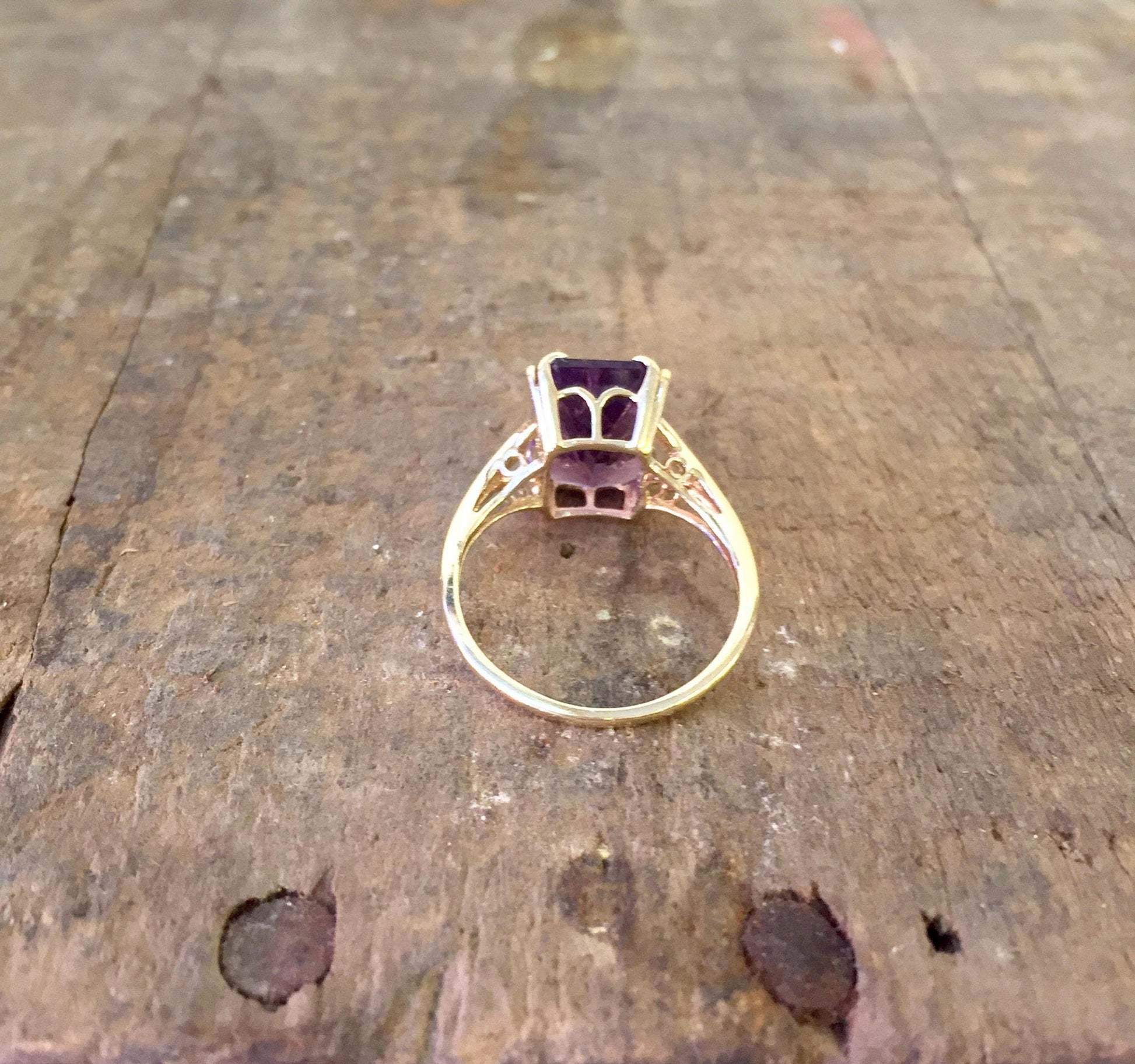 14 karat yellow gold ring with emerald cut amethyst gemstone on rustic wooden surface