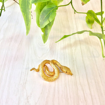 Gold tone coiled snake brooch pin on wooden background with green leaves, vintage costume jewelry gift idea