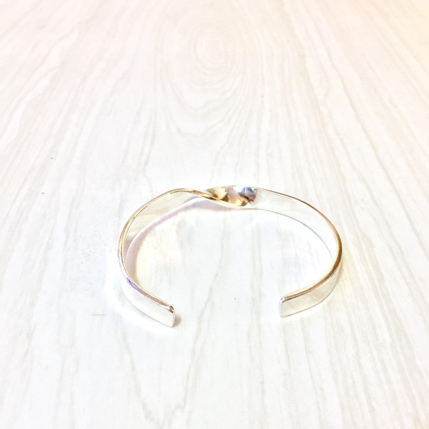 Simple twist sterling silver cuff bracelet on white wooden background, minimalist 925 jewelry with classic and timeless design.