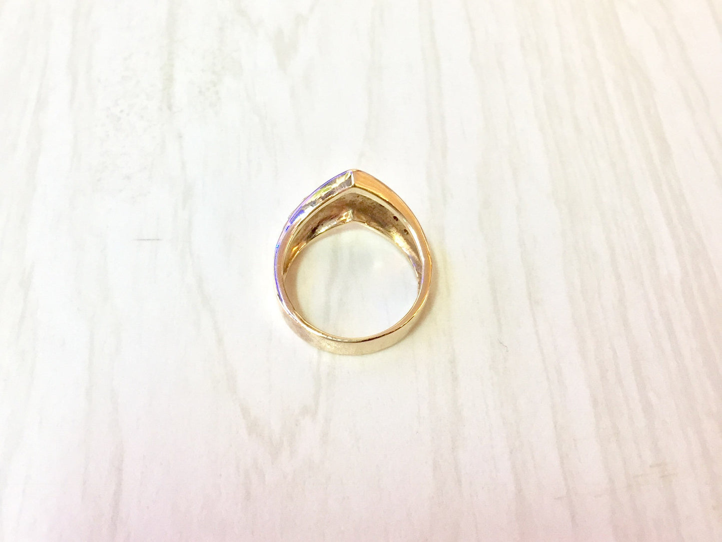14K yellow gold chevron V-shaped ring with diamonds on light wooden background, top view