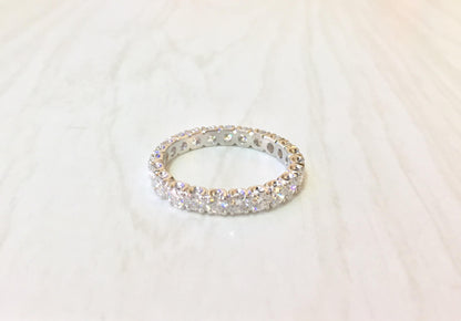 14 karat white gold eternity wedding band ring with round cut diamonds set all around the band, photographed on a light background.