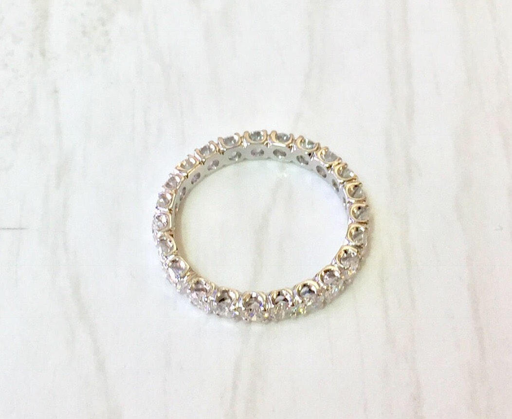 14 karat white gold diamond eternity band wedding ring with round brilliant cut diamonds set all around the band on a white fabric background