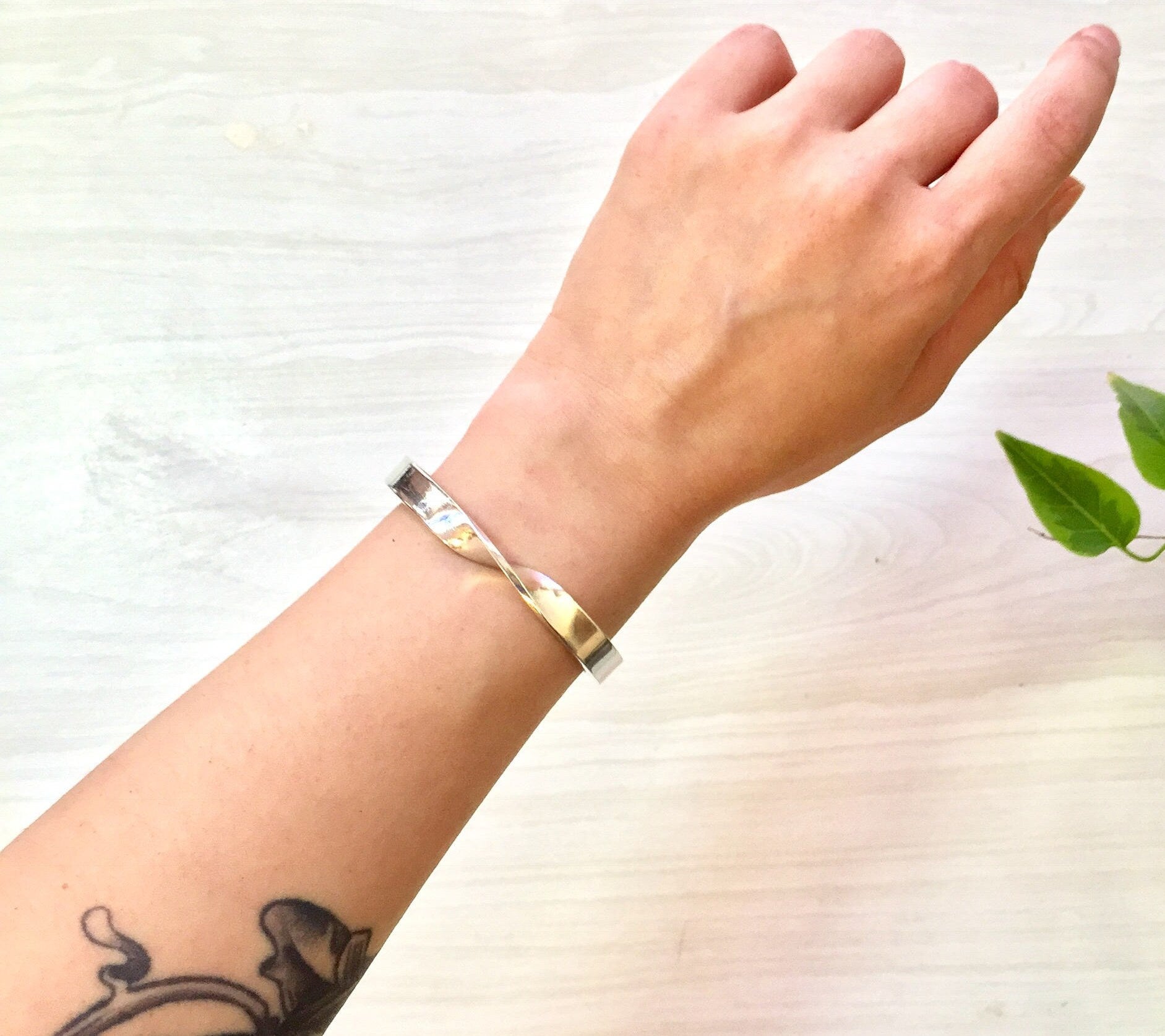 Sterling silver twist cuff bracelet on wrist with leaf in background