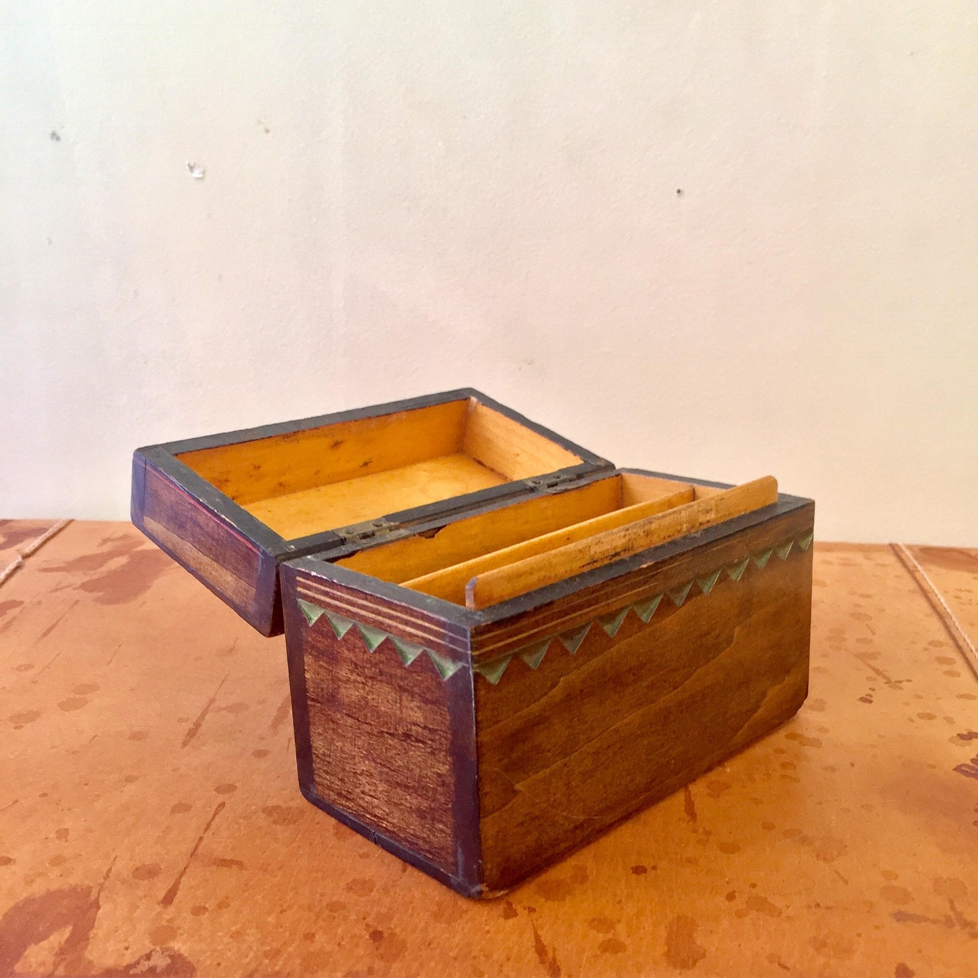 Rustic hand-carved wooden box with colorful geometric patterns, featuring a sliding lid and yellow interior, sitting on a wooden surface.