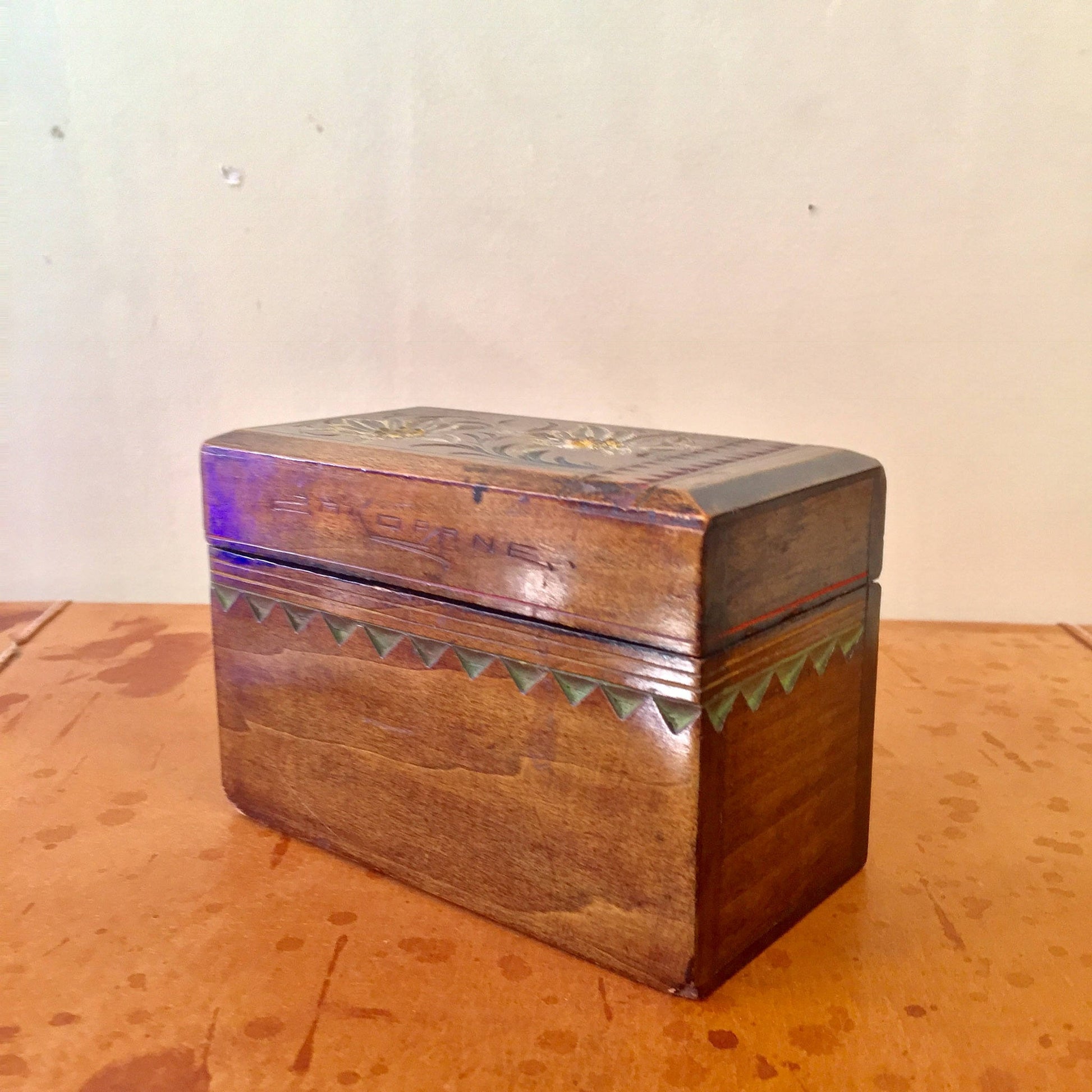 Antique wooden box with hand-carved floral designs and colorful painted accents, sitting on a rustic wooden surface.