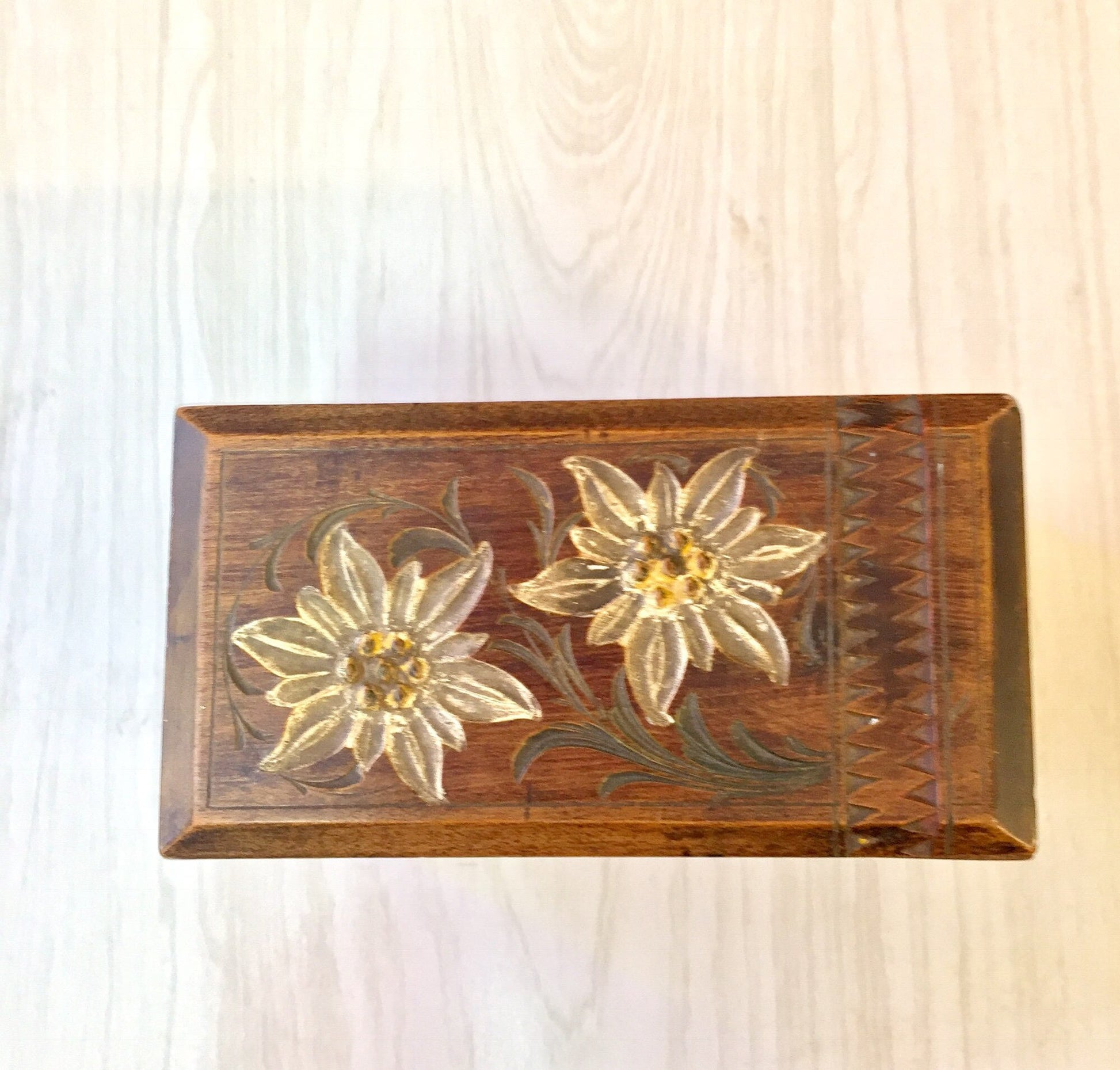 Carved wooden box with floral design on lid featuring two white flowers against a dark stained wood background.