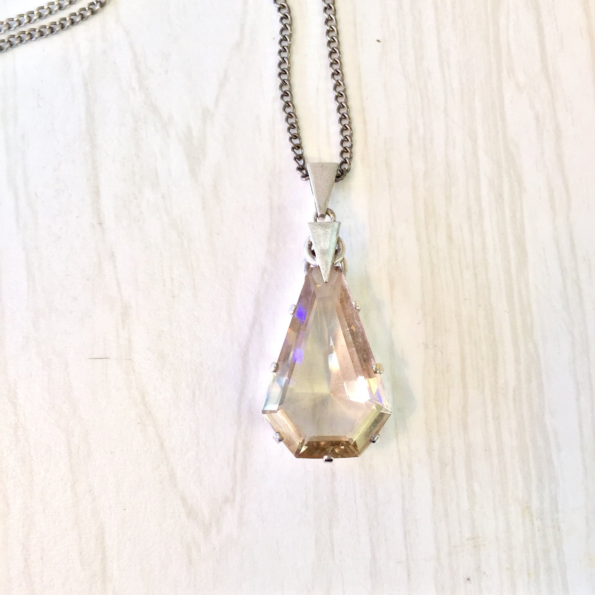 Antique silver chain necklace with a large, multifaceted smoky quartz pendant displaying iridescent hues against a light wooden background.