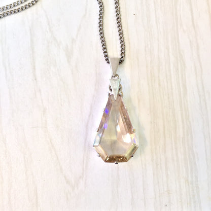 Antique silver chain necklace with a large, multifaceted smoky quartz pendant displaying iridescent hues against a light wooden background.