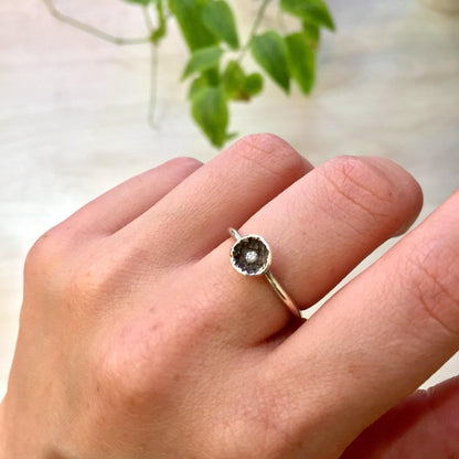 Sterling silver ring with round black diamond center stone worn on hand next to plant branch