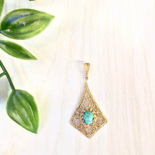 14K yellow gold filigree pendant with turquoise gemstone, displayed with green leaves on a white background.