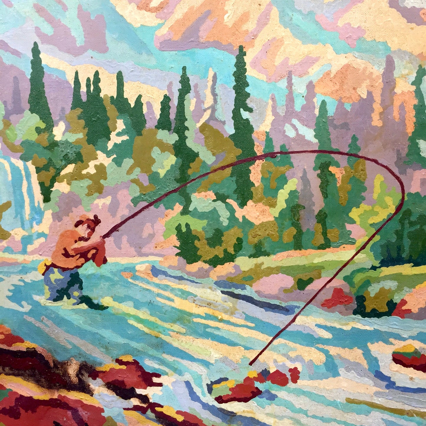 Colorful vintage paint-by-numbers oil painting of a person fishing in a mountain stream surrounded by pine trees, with a wooden frame.