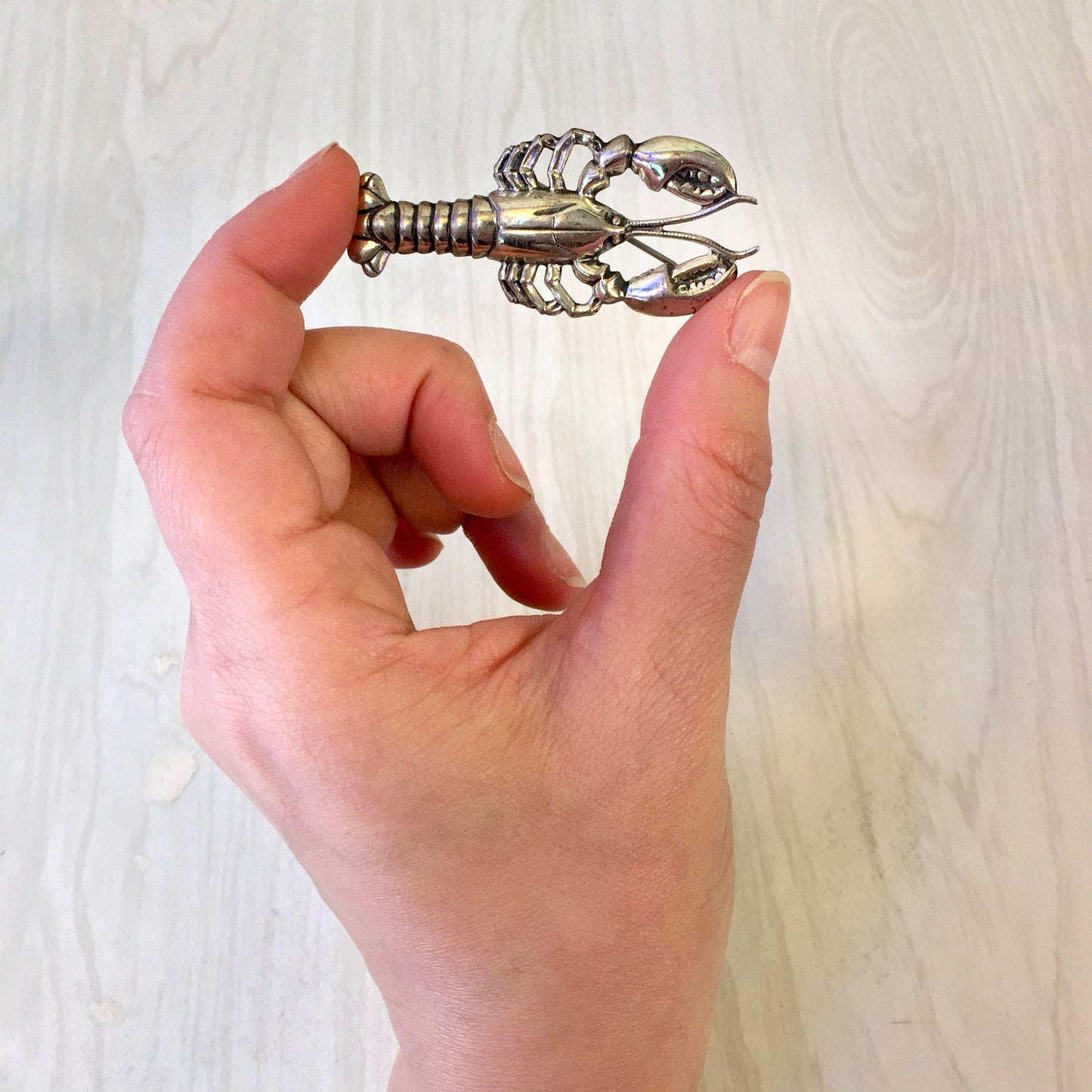 Vintage sterling silver lobster brooch pin held in hand, showing intricate detailing on the lobster jewelry piece against a light wooden background.