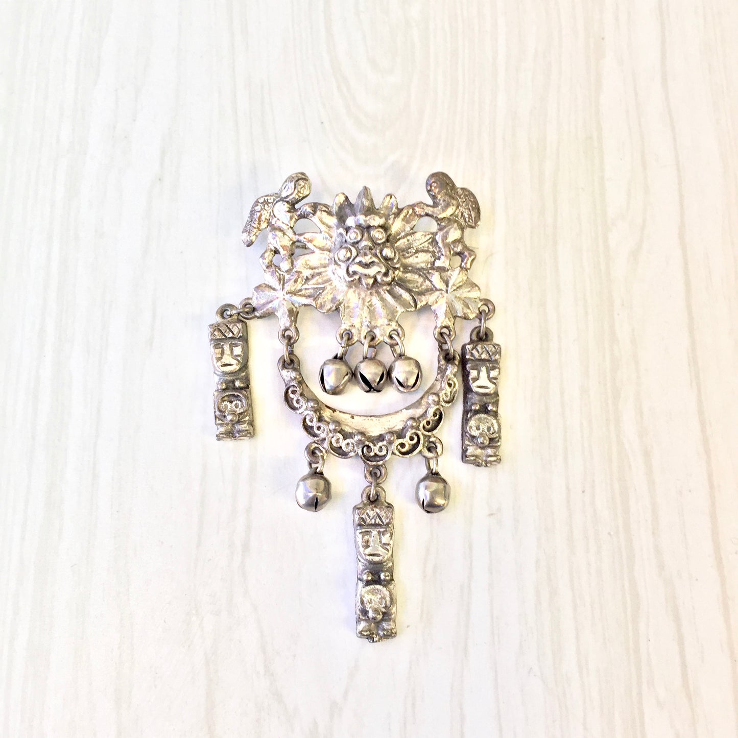 Vintage silver tone Peruvian art brooch pin with intricate floral and bell design, featuring dangling charms and faux pearl accents, making a bold statement jewelry piece suitable as a costume accessory or special gift.