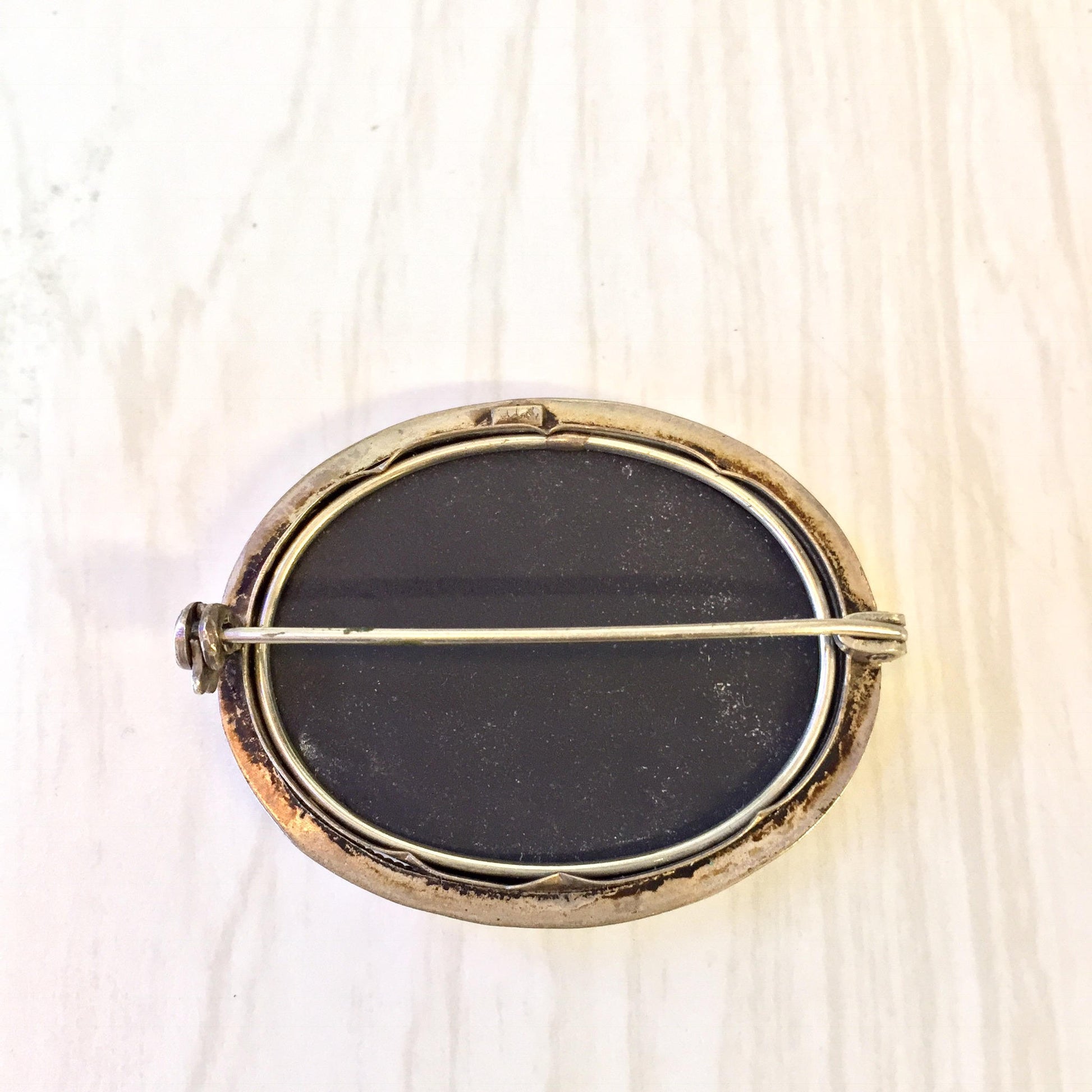 Vintage sterling silver brooch featuring an oval black stone inlay surrounded by a gold-toned metal frame, set against a light wooden background.