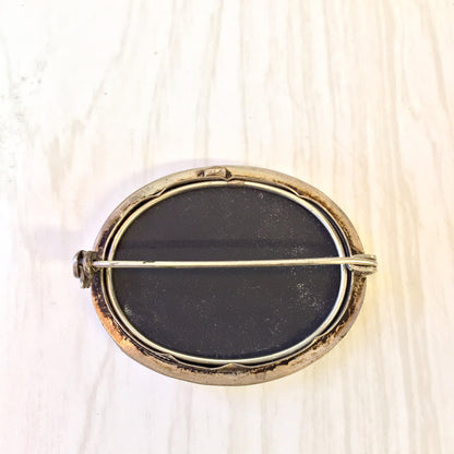 Vintage sterling silver brooch featuring an oval black stone inlay surrounded by a gold-toned metal frame, set against a light wooden background.