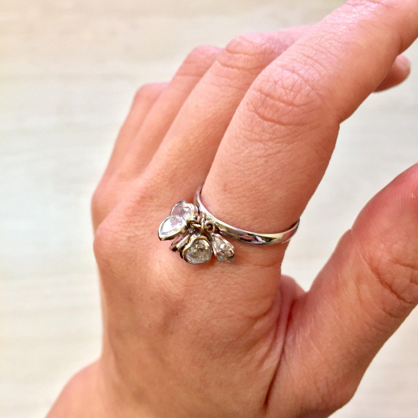 14K white gold ring with dangling cubic zirconia heart charms on a person's finger, perfect holiday gift idea for her
