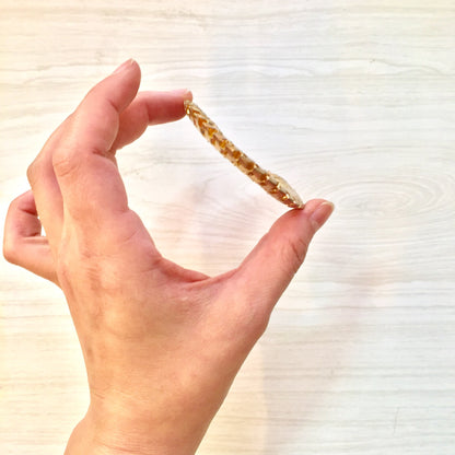 A hand holding a small, gold-toned hoop earring against a light wooden background, demonstrating the size and style of the vintage fashion earrings.