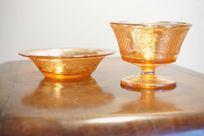 Set of two vintage orange carnival glass dishes with iridescent finish, featuring an intricate embossed floral pattern on a wooden surface.