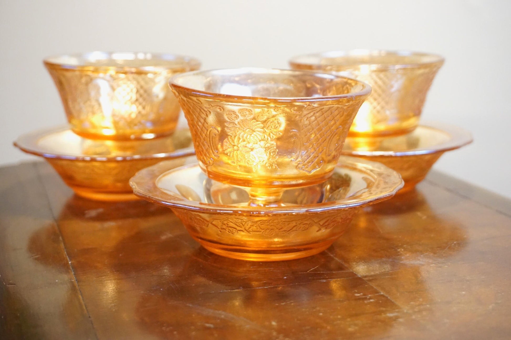 Set of three vintage orange carnival glass dessert dishes with an iridescent shine, stacked on a wooden surface.