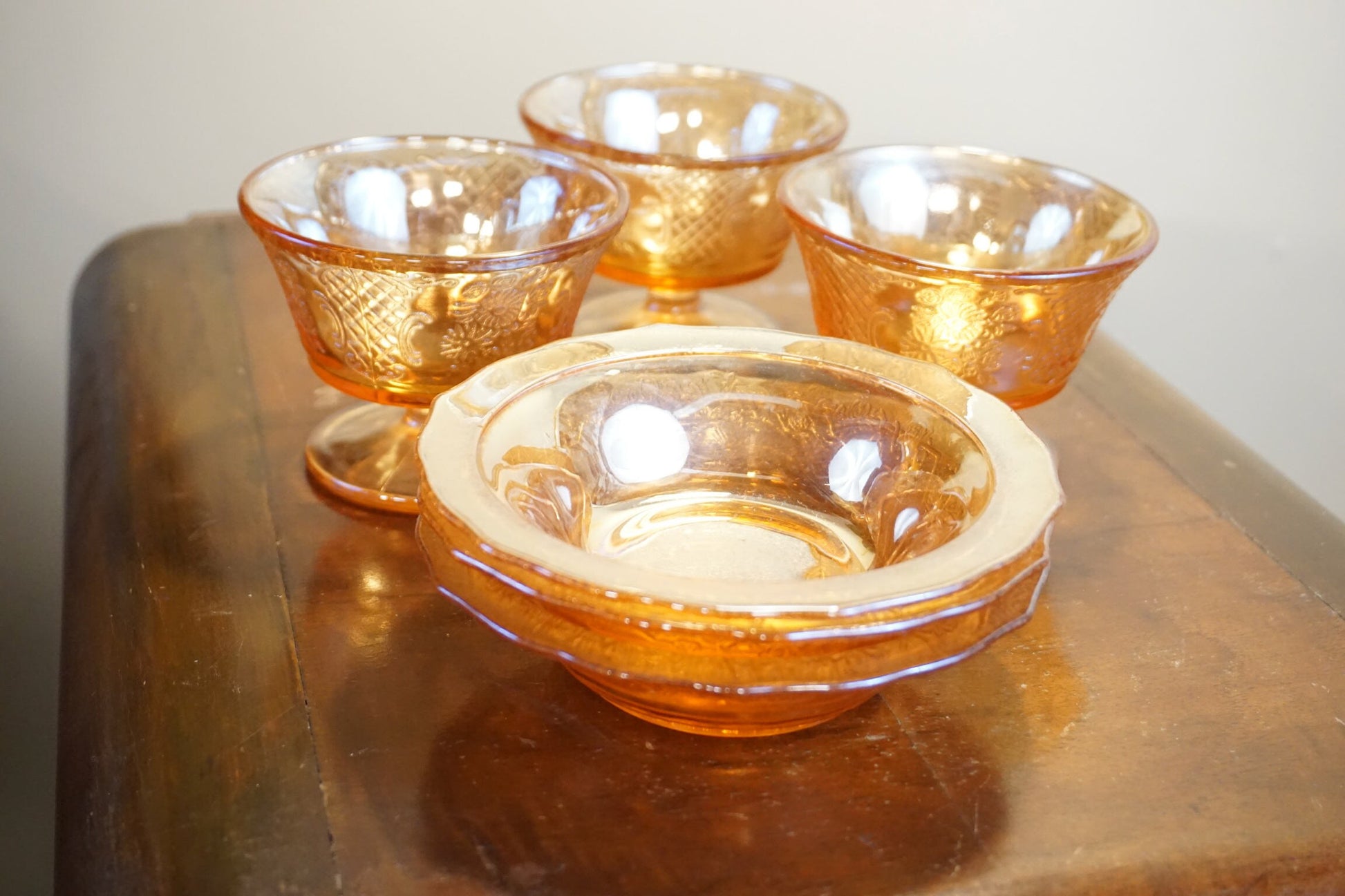 Set of four vintage orange iridescent carnival glass dessert dishes on a wooden table, the glass bowls have a swirled, textured pattern that catches the light