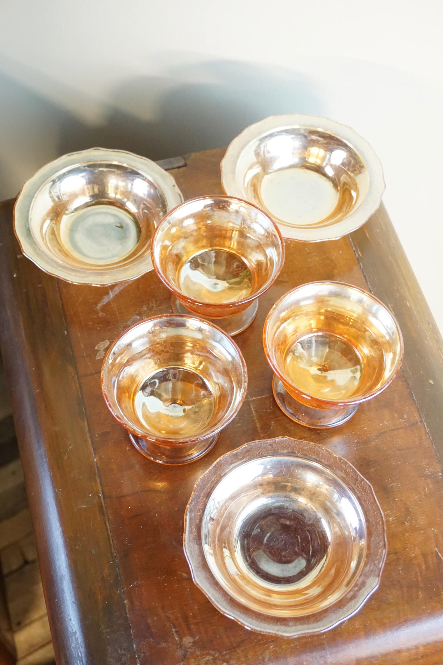 Set of six vintage orange opalescent carnival glass dessert dishes on a wooden surface, showing their iridescent sheen and unique shape from above.