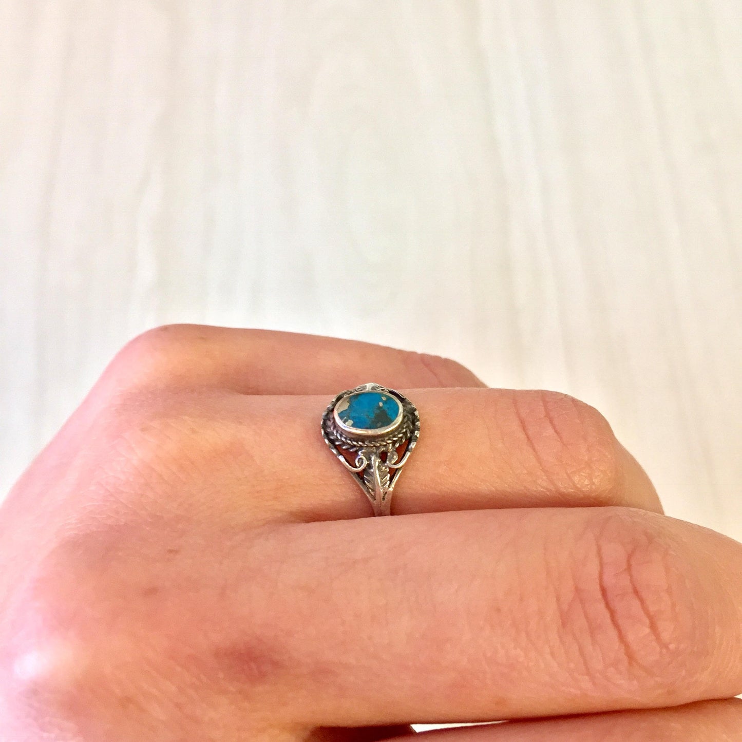 Vintage sterling silver ring with turquoise stone in ornate setting on a hand, showcasing southwestern style jewelry design