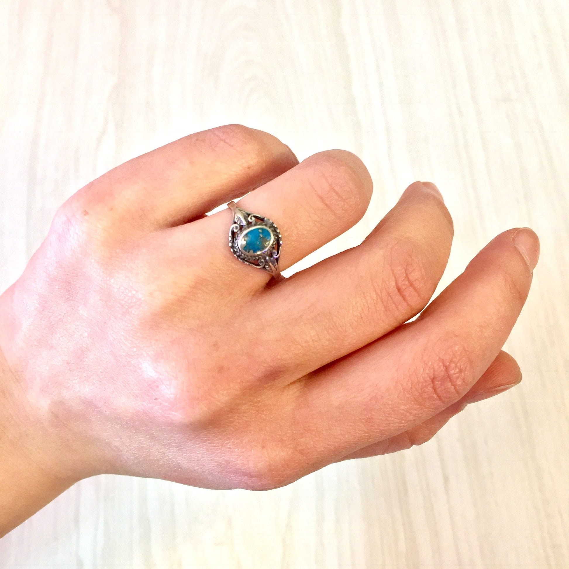 Vintage sterling silver ring with an oval turquoise stone set in an ornate silver setting, shown on a hand against a light wooden background.