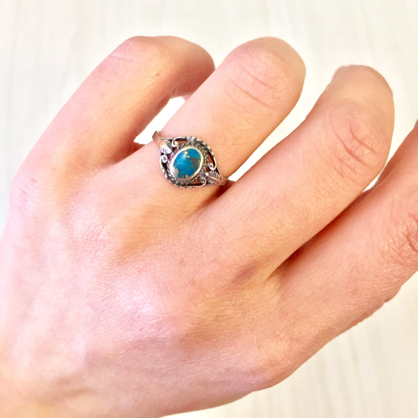 Vintage sterling silver ring with turquoise stone on a hand, showcasing southwestern jewelry design with an oval blue turquoise cabochon set in an intricate silver setting.