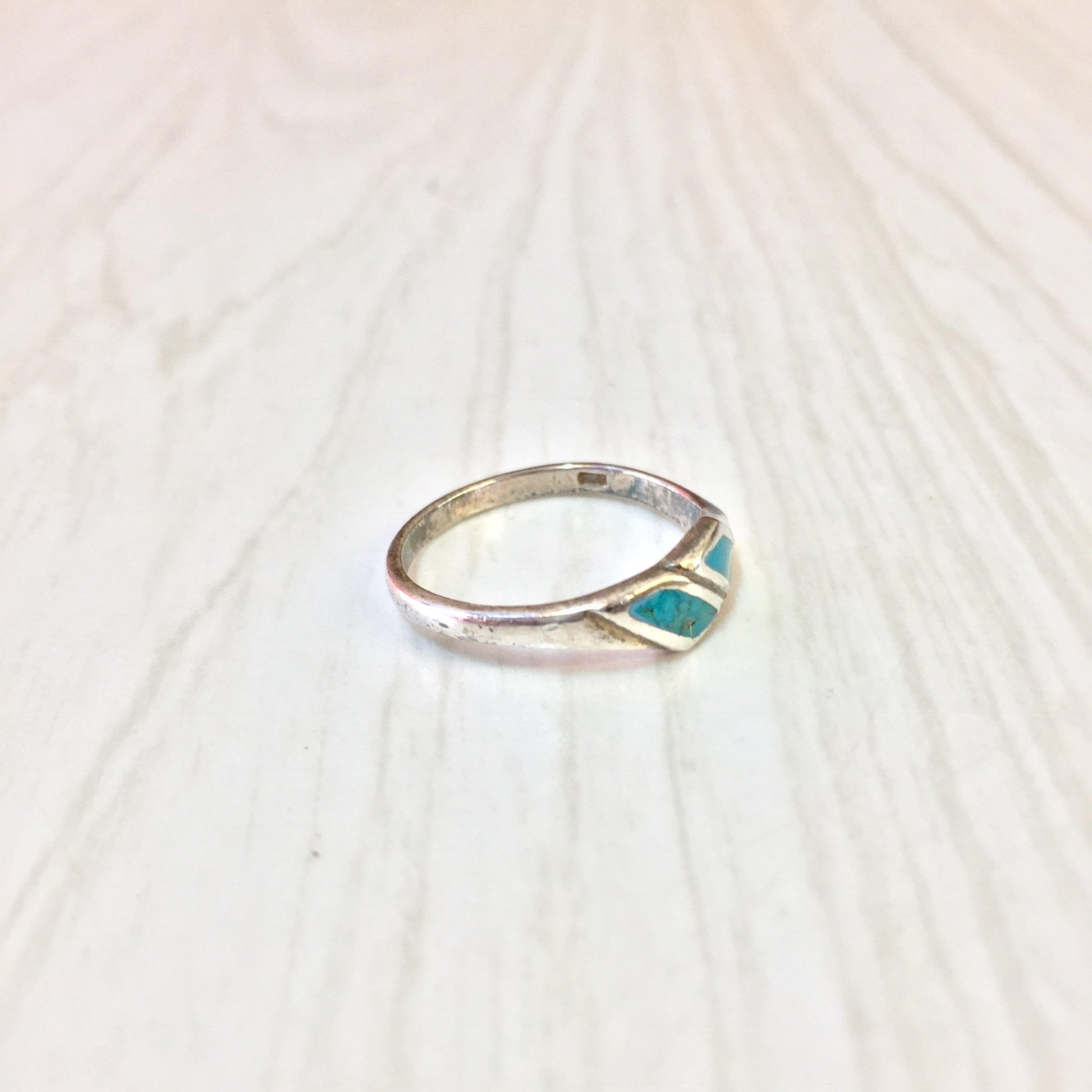 Vintage sterling silver ring with turquoise stone in a southwestern style setting on a light wooden surface