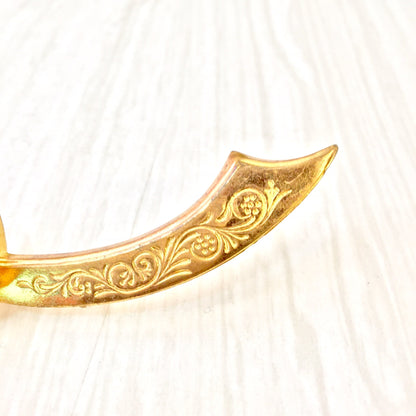 Gold tone vintage sword brooch with ornate engraved design and gemstone accents, curved scimitar shape, costume jewelry pin from historical era.