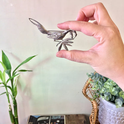 Vintage sterling silver bird brooch by Guglielmo Cini for Gump's, held by a hand next to a potted plant, showcasing the intricate detailing and design of the silver bird pin against a neutral background.