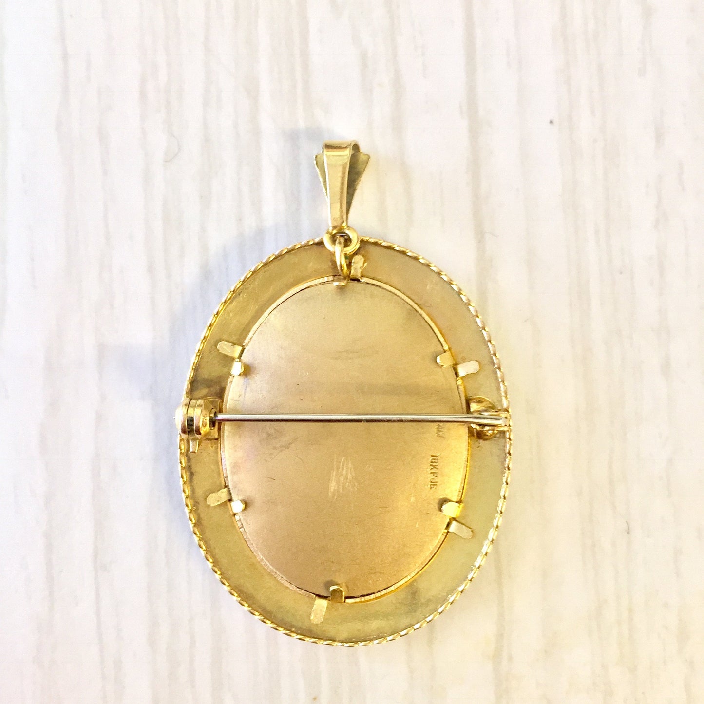 18 karat gold Victorian oval locket brooch pendant with intricate engraved border design on a light wood background