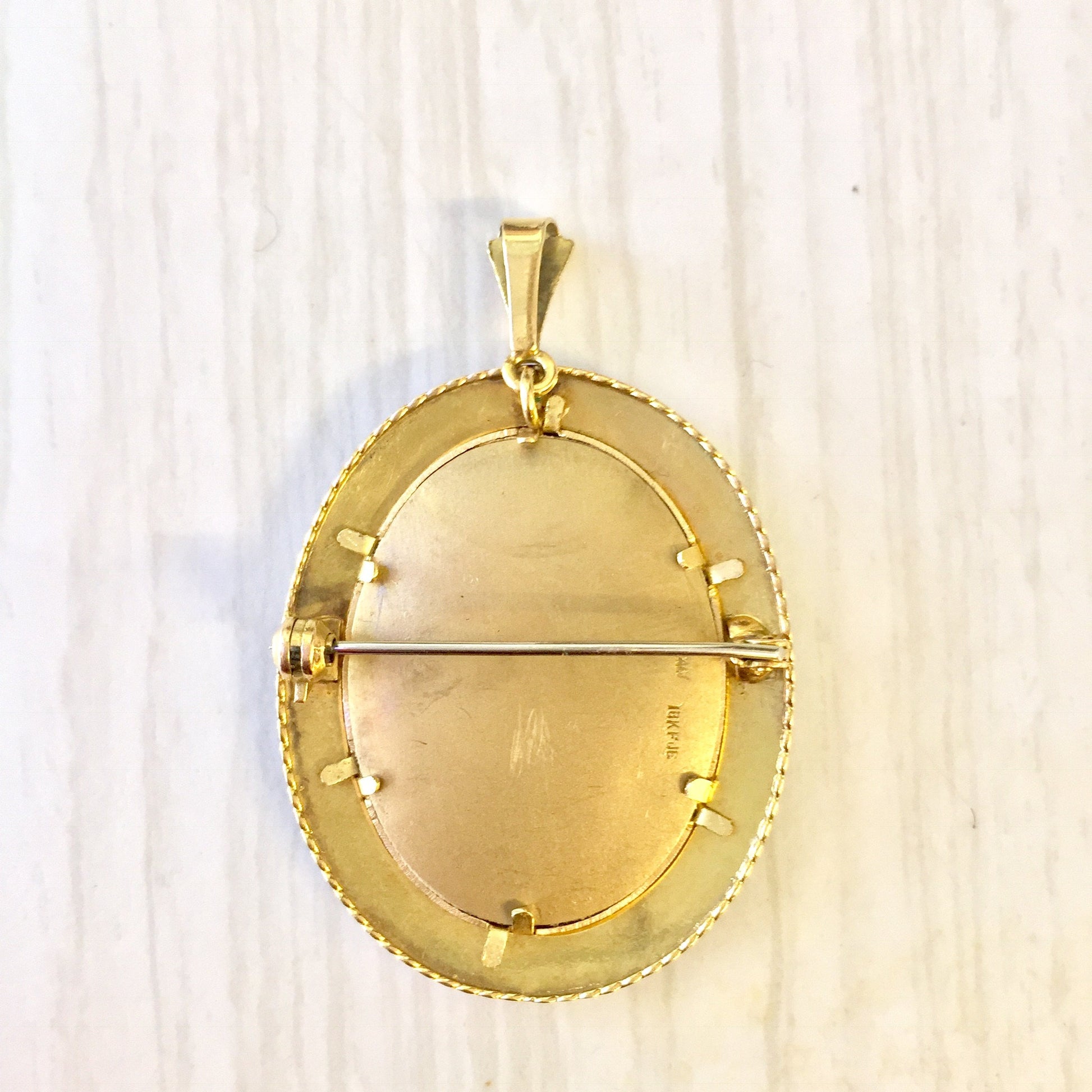 18 karat gold Victorian oval locket brooch pendant with intricate engraved border design on a light wood background