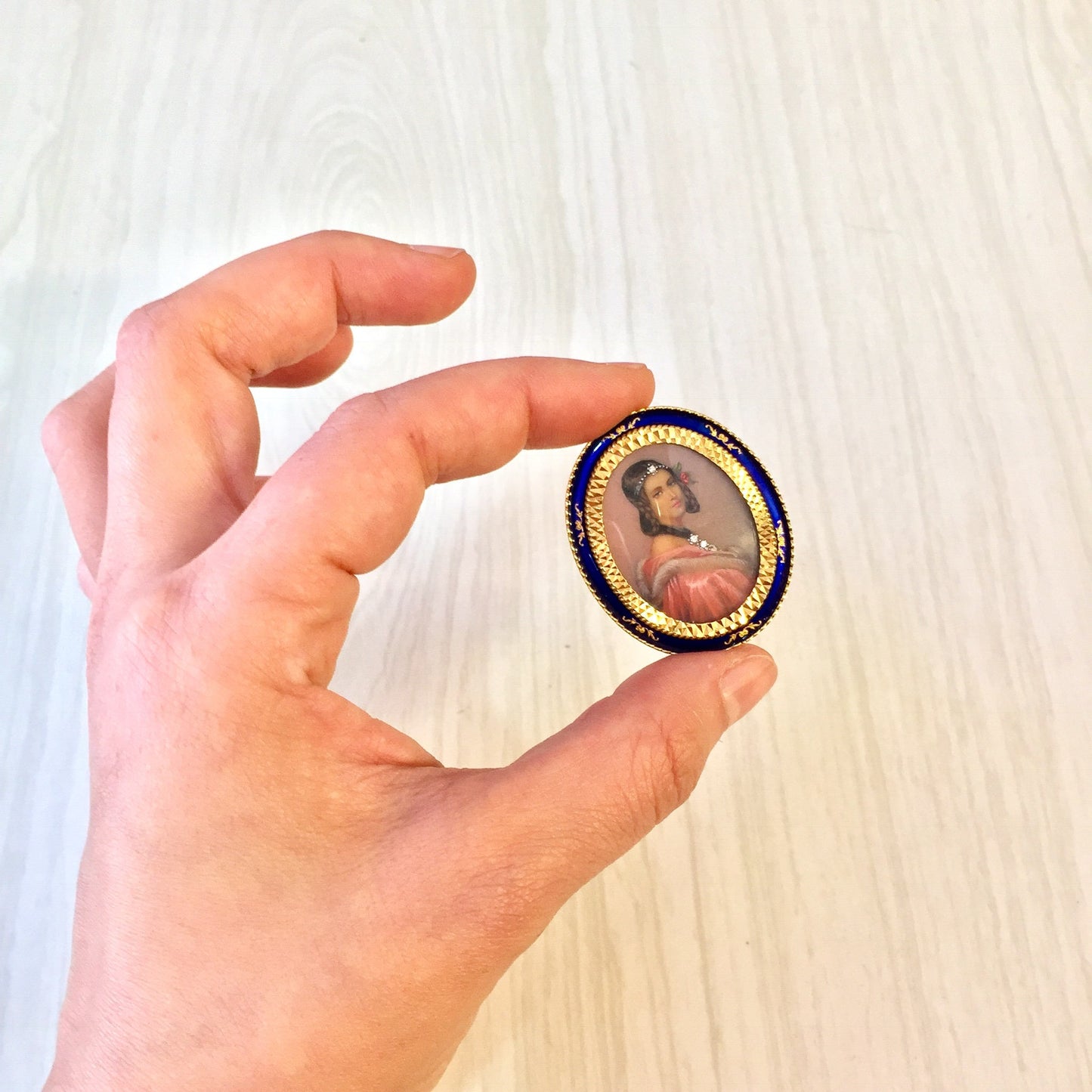 18K gold Victorian brooch pendant featuring an antique cameo portrait framed by diamonds, held in a hand against a light wooden background.