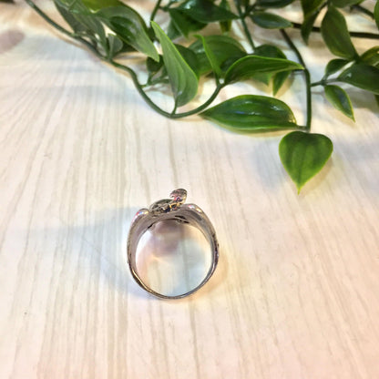 Vintage sterling silver statement ring featuring an eagle and skull design, displayed on a wooden surface with green foliage in the background.