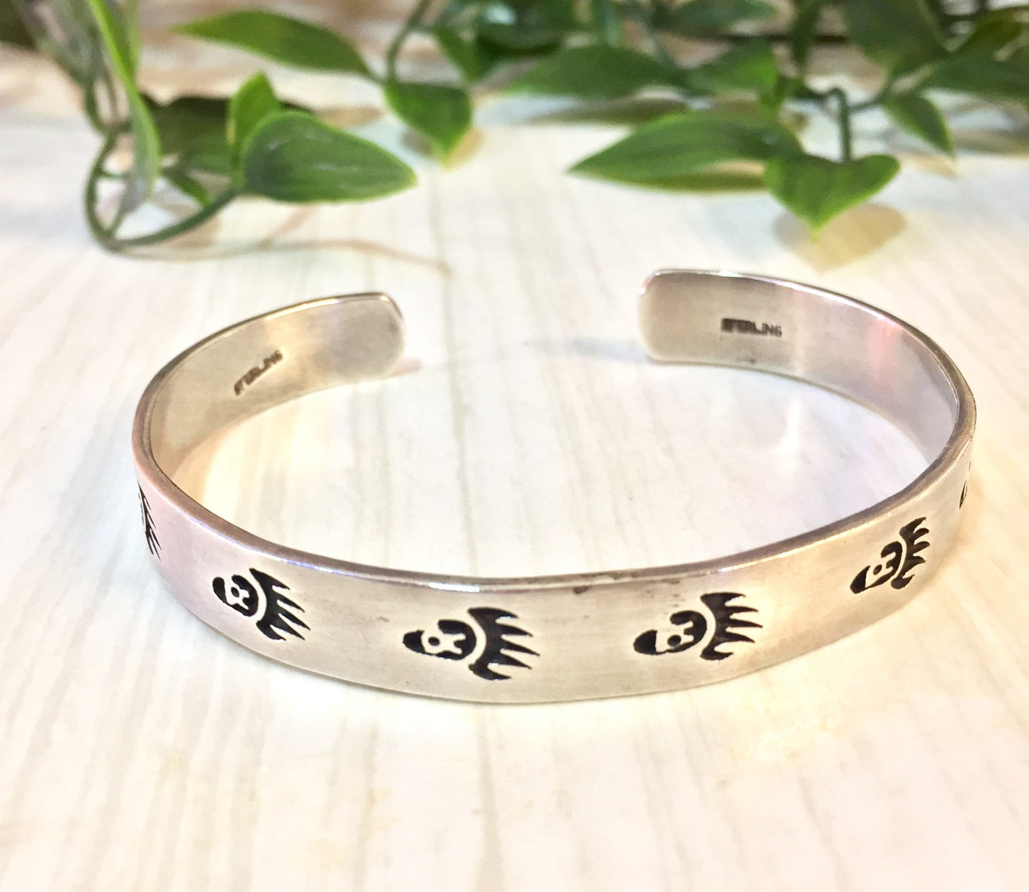 Vintage silver cuff bracelet with bear paw design, displayed with greenery on textured background, perfect Native American inspired jewelry gift for Valentine's Day.