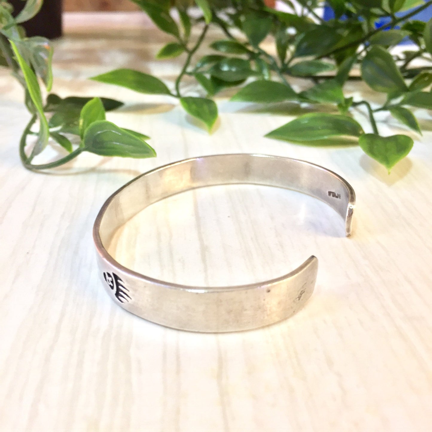 Vintage silver bear paw cuff bracelet displayed on wooden surface with plant in background