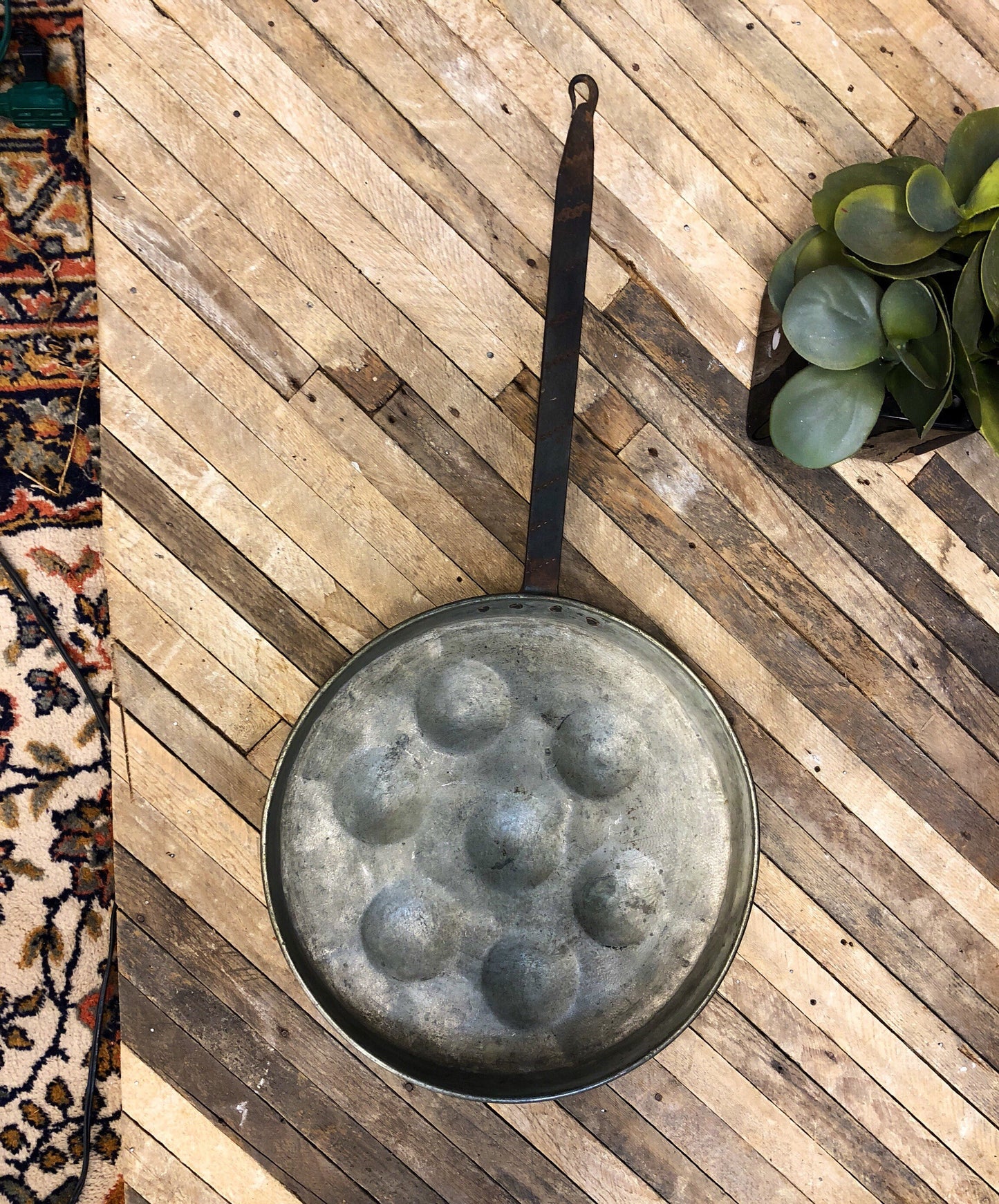 Antique copper pan with dimpled surface for poaching eggs on rustic wooden deck with ornate rug and succulent plant, vintage kitchenware and folk art home decor