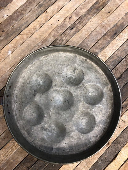 Antique copper pan on wooden surface, used for poaching eggs. Rustic, hand-made kitchen decor from a bygone era, showcasing vintage country folk art style.