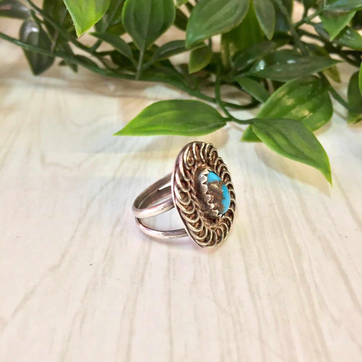 Vintage sterling silver ring with turquoise stone on wooden surface next to green plant leaves