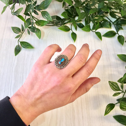 Vintage silver and turquoise statement ring on a hand surrounded by green leaves, sterling silver jewelry with blue gemstone