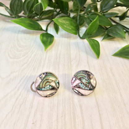 Vintage silver mosaic earrings with abalone mother of pearl inlay, displayed on a light wooden surface with green plant leaves in the background.